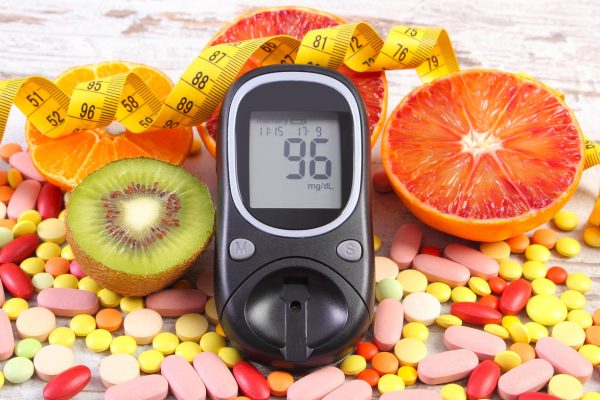 Glucose meter with result of measurement sugar level, tape measure, fresh fruits and medical tablets or supplements, concept of diabetes, slimming, healthy lifestyle and nutrition
